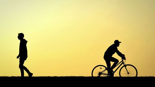 Woman riding bicycle on road at sunset