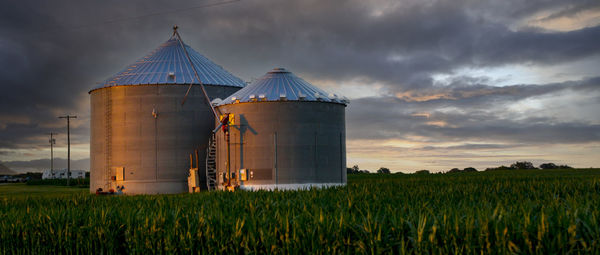 Sunsetting on two grain silos in a field.