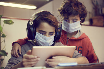 Low angle view of brothers wearing masks using digital tablet on table