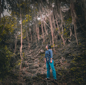 Man standing by tree trunks in forest