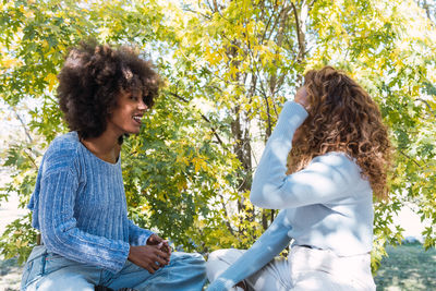 Two female afro american friends with blue jumper having a conversation outdoors while smiling