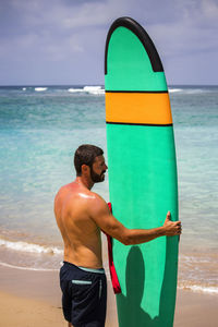 Shirtless man with surfboard standing at beach