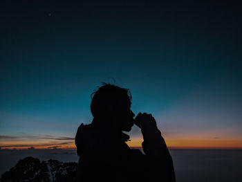 Silhouette man drinking against sea during sunset