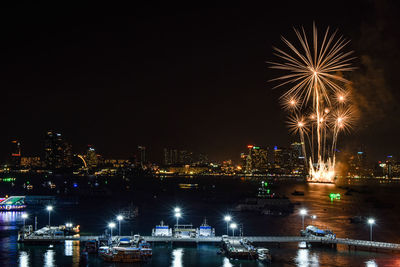 Firework display over river against illuminated buildings in city at night