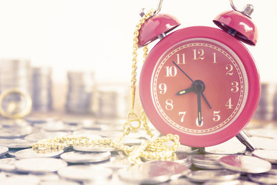 Close-up of alarm clock on coins with gold chain at table