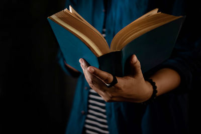 Midsection of person reading book against black background