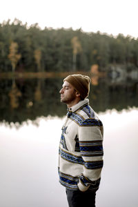 Side view of man with hand in pocket standing by lake