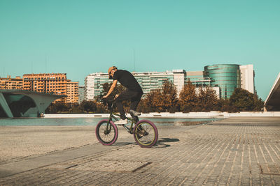 Man riding bicycle in city against clear sky