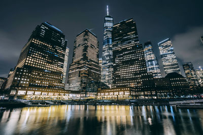 Illuminated modern buildings by river against sky in city at night