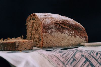 Close-up of bread with knife on table against black background