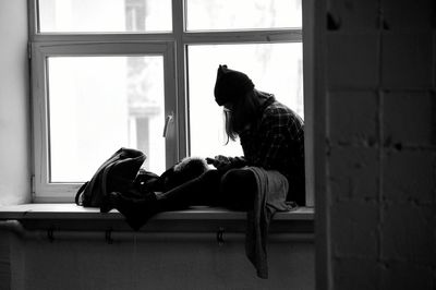 Woman using mobile phone while sitting on window sill