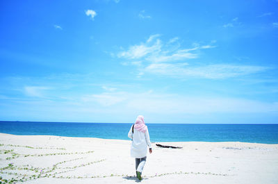 Rear view of woman standing on beach against blue sky