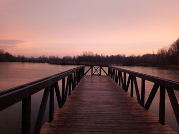 Wooden bridge over lake against sky during sunset