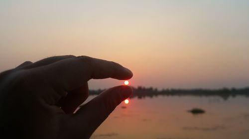 Midsection of man holding sun against sky during sunset
