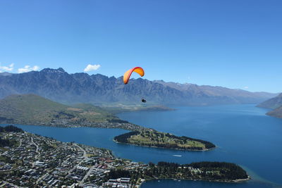 Person paragliding over mountains against blue sky