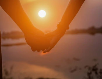 Silhouette hand against orange sky during sunset