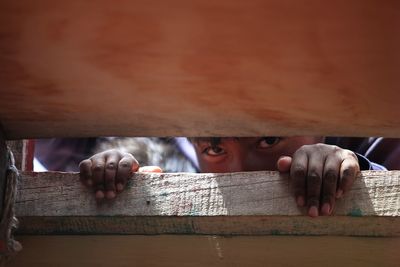 Close-up portrait of boy peeking through wooden bamboo