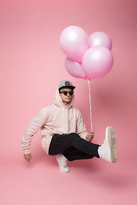 Man in sunglasses holding helium balloons against pink background