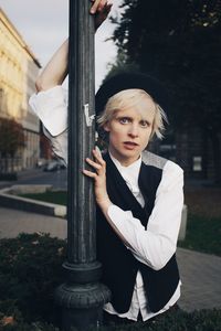 Portrait of young woman standing by pole against trees