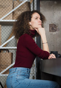 Beautiful serious curly woman in casual clothes listening headphones while sitting at table in cafe.