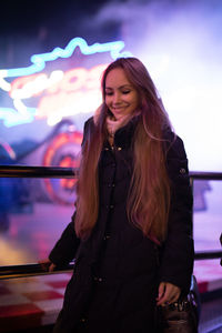 Smiling young woman standing against illuminated wall