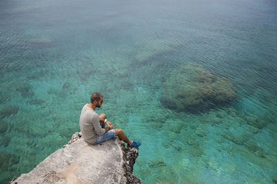 High angle view of mid adult man looking at sea while sitting on rock