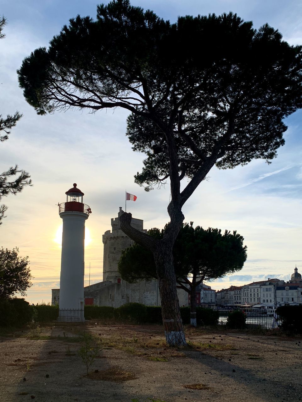 LIGHTHOUSE AMIDST TREES AND BUILDINGS AGAINST SKY AT SUNSET