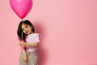 Portrait of young woman with balloons against pink background