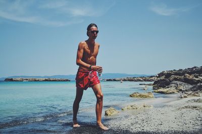 Portrait of shirtless man walking on shore at beach sky