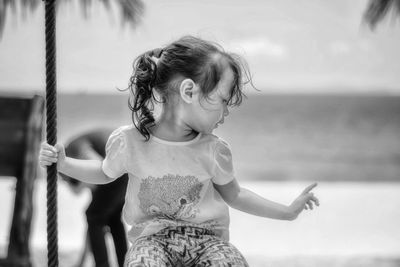 Cute girl looking away while sitting on swing at beach