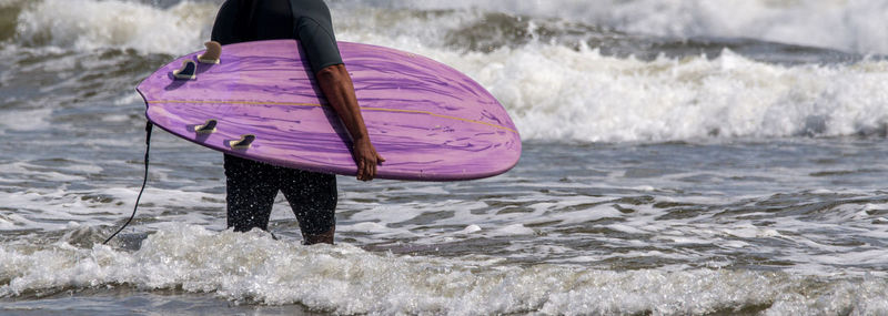 Rear view of a man carrying his purple surfboard into the ocean at gilgo beach long island new york.