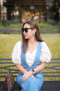 Beautiful woman wearing sunglasses sitting on bench at park