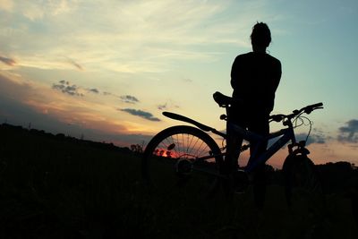 Silhouette man with bicycle on field against sky during sunset