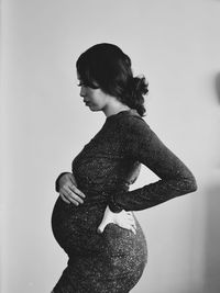 Side view of pregnant woman standing against wall