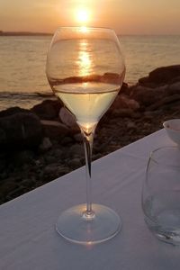 Wineglass on table by sea against sky during sunset