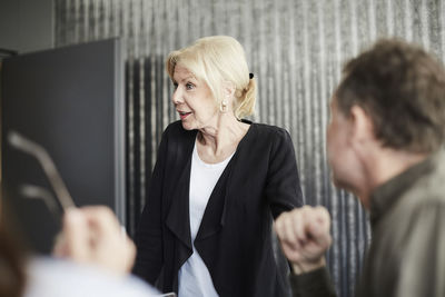 Senior female professional standing with colleagues in board room during meeting