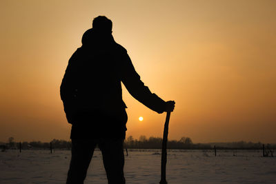 Silhouette man standing at lakeshore against orange sky