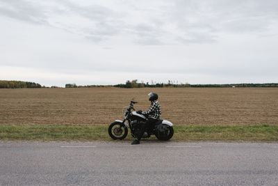 Man sitting on motorcycle at roadside against sky