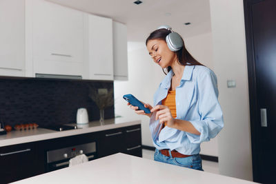 Portrait of young woman using mobile phone while standing in office