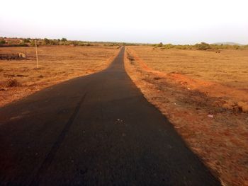 Empty road amidst field against clear sky