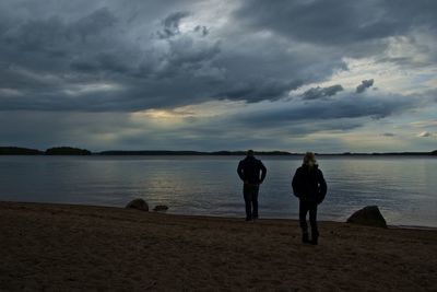 Silhouette of woman standing on beach against cloudy sky