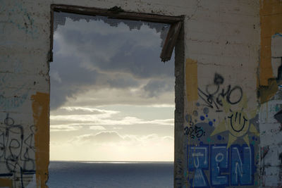 Graffiti on wall by sea against sky