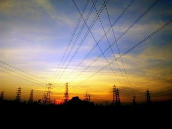 Low angle view of electricity pylon against sky at sunset