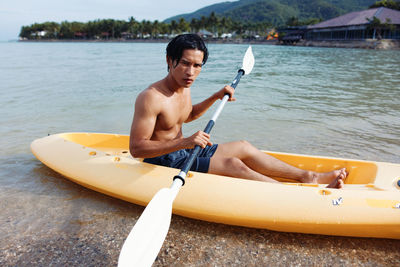 Rear view of shirtless man kayaking in sea