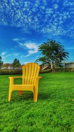 Empty bench on field by trees against sky