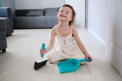 Cute european child with blue scoop for garbage and brush for sweeping floor helps