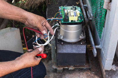 Hands of an electrician with multimeter probe at electric board panel.