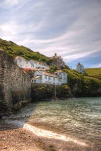 View of houses by calm sea against cloudy sky