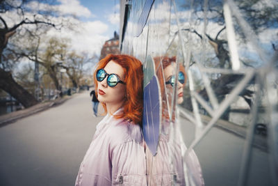 Redhead young woman wearing sunglasses while leaning on mosaic wall by street