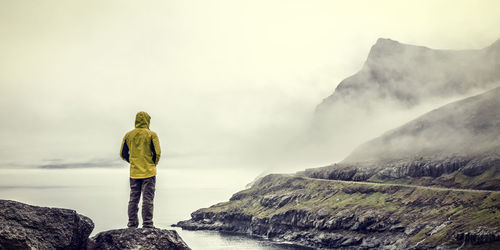 Rear view of man standing on rock against sky